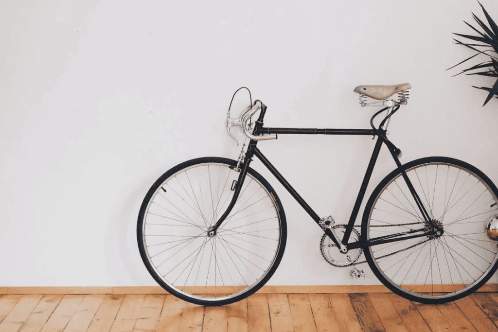 bicicleta negra de paseo apoyada en pared blanca en interior con suelo de madera
